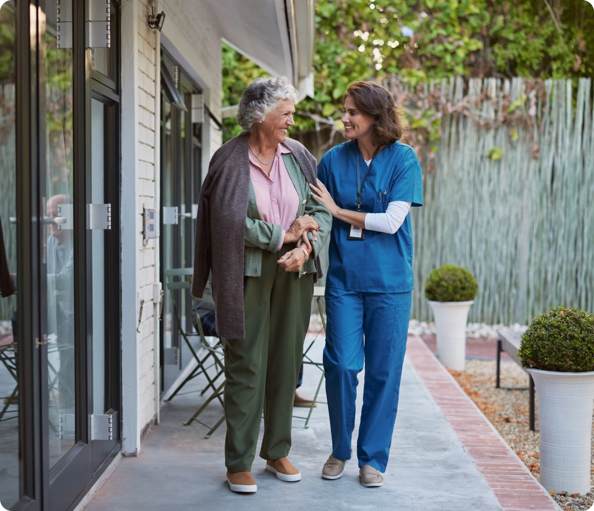 Caregiver supporting elderly woman on patio